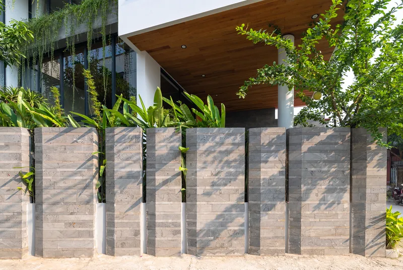 Layered concrete fence with vertical steel fins casting shadows beside planted beds and timber entry canopy