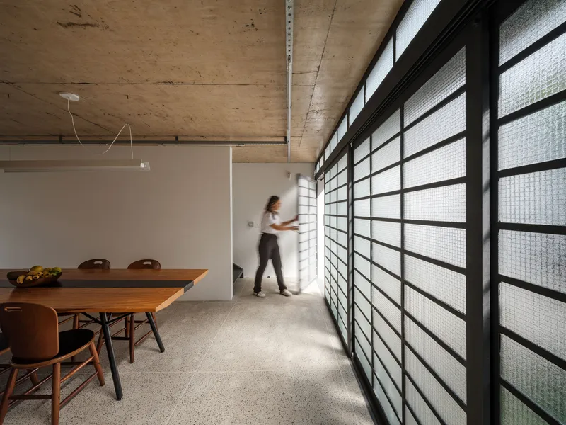 Interior with full-height glass block wall, figure walking in blurred motion, exposed concrete ceiling, and terrazzo floor