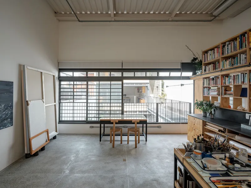 Studio workspace with gridded windows, plywood shelving, and a corrugated metal ceiling under natural light