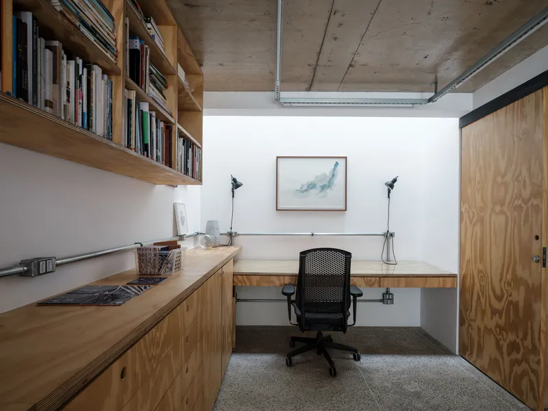 Compact work area with built-in plywood desk, exposed concrete ceiling, and floating timber shelves