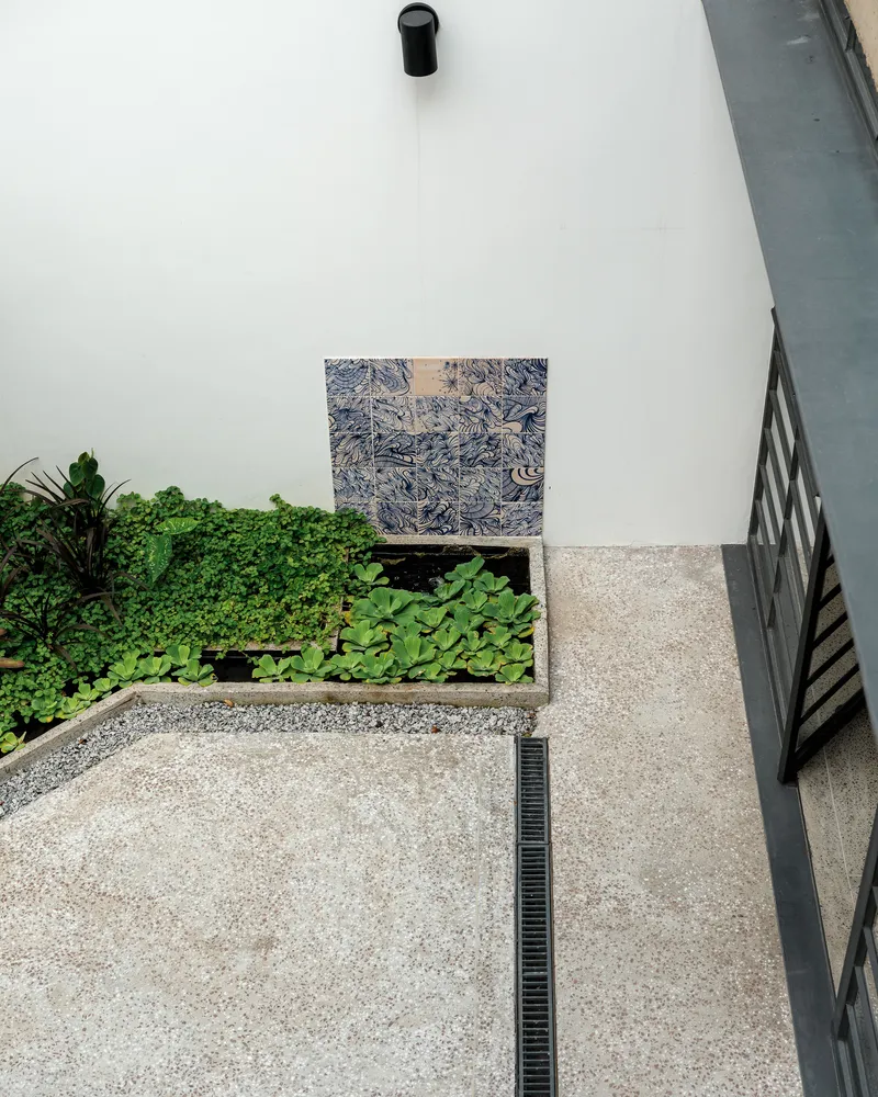 Top-down view of courtyard with planted bed, exposed aggregate paving, and patterned tile wall panel