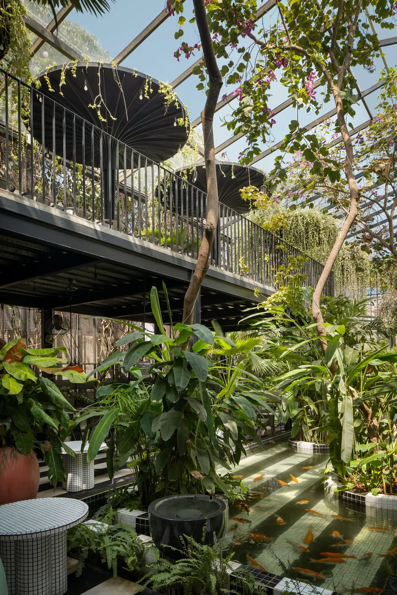 Upper level walkway with corrugated metal balustrades above a planted courtyard with tropical foliage