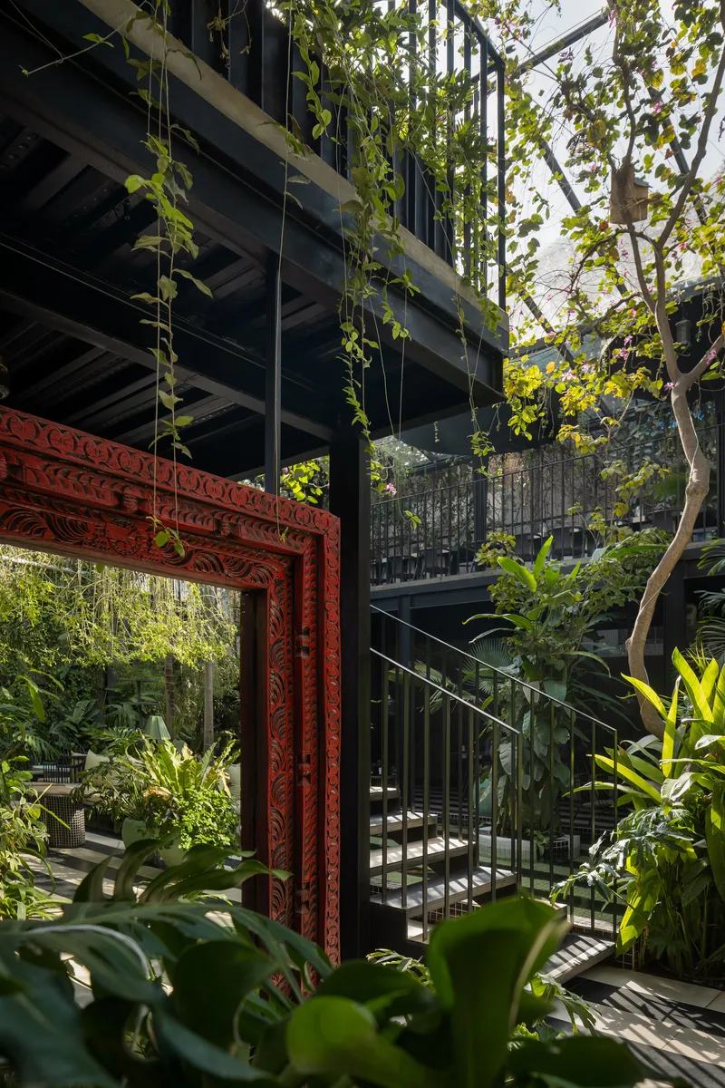 Carved red timber portal framing a courtyard garden beneath a steel-framed upper level with cascading vines