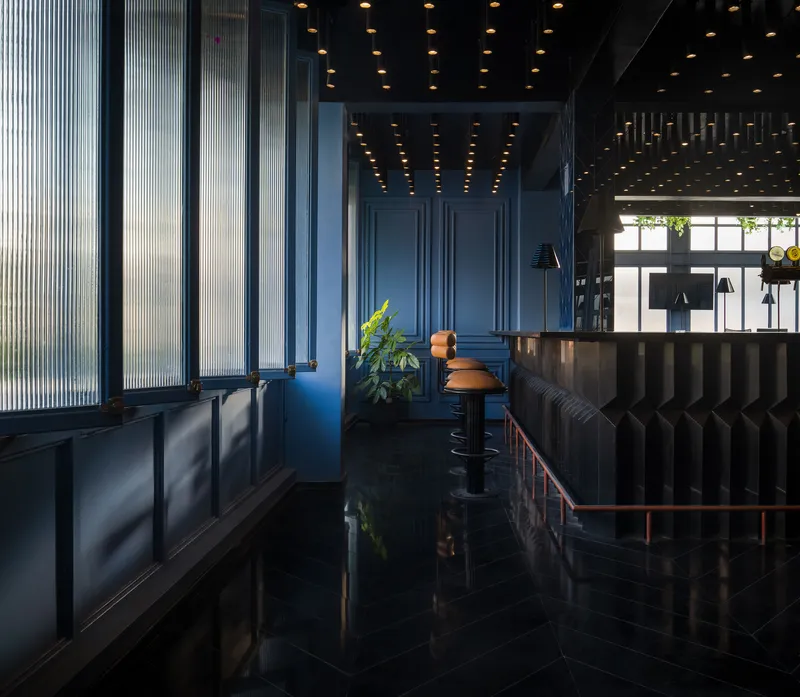 Blue ribbed screen wall beside a ribbed banquette under a recessed ceiling with pendant lights