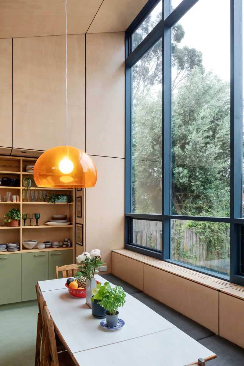 This architectural image showcases a modern dining room with a minimalist design. The room features plywood walls and built-in seating, complemented by a large