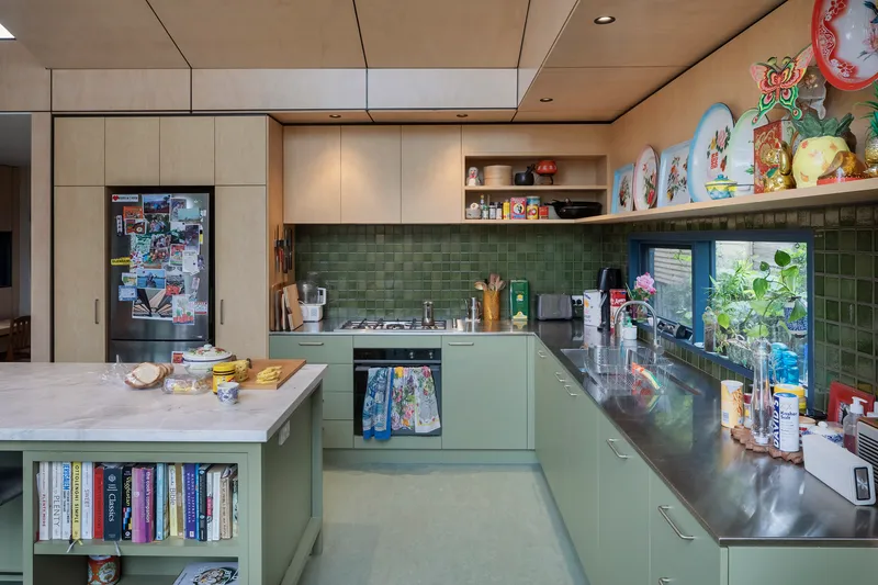 This image showcases a modern kitchen with a unique blend of materials and colors. The kitchen features green cabinets, a stainless steel countertop, and a plyw