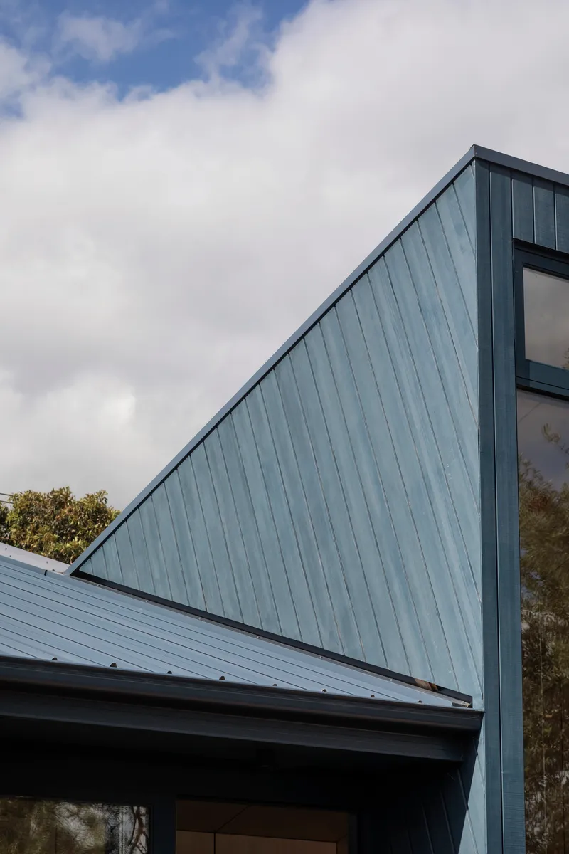 Angled metal roof cladding rising to form a gable under cloudy sky