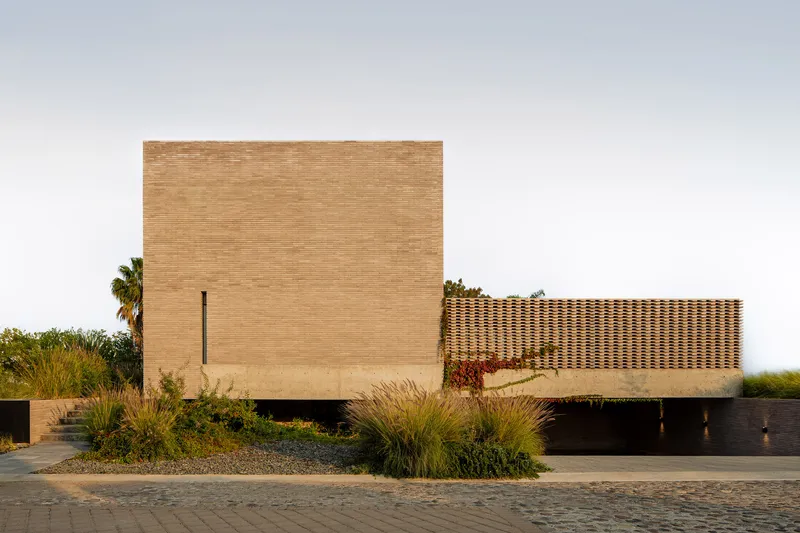 Street facade with horizontal brick coursing and perforated screen wall flanked by native grasses