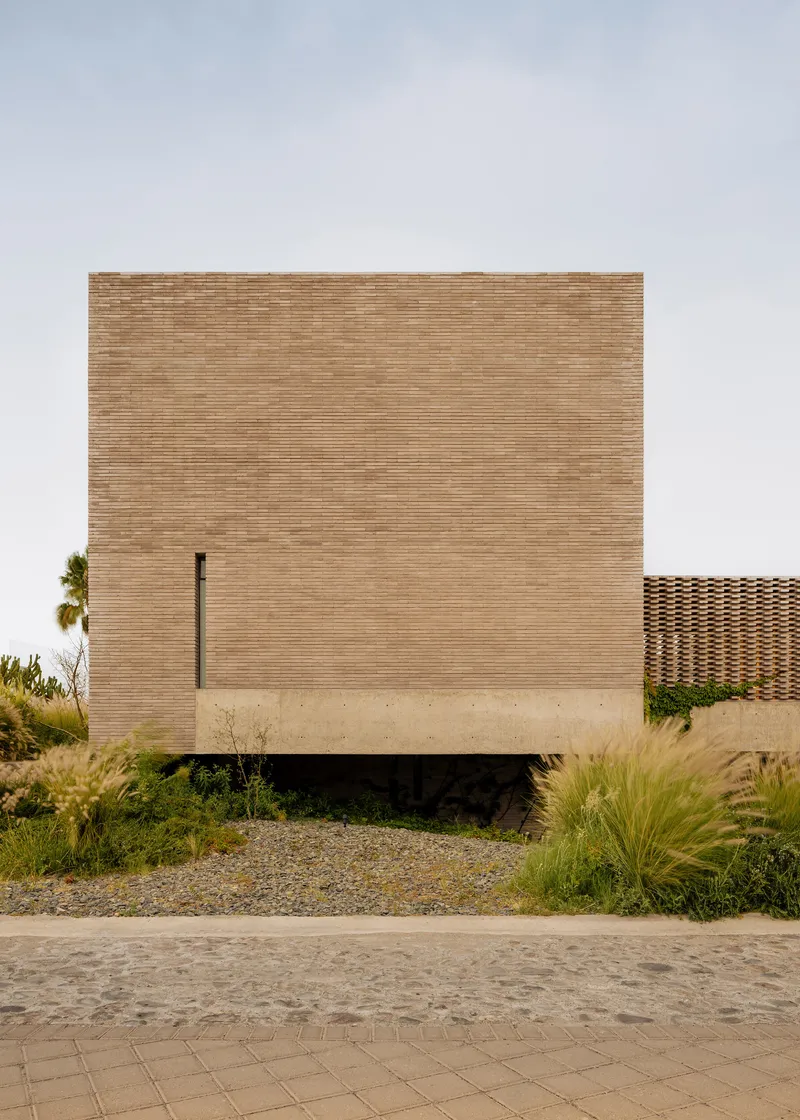 Front facade of horizontal brick volume with narrow vertical window slot and planted landscape bed