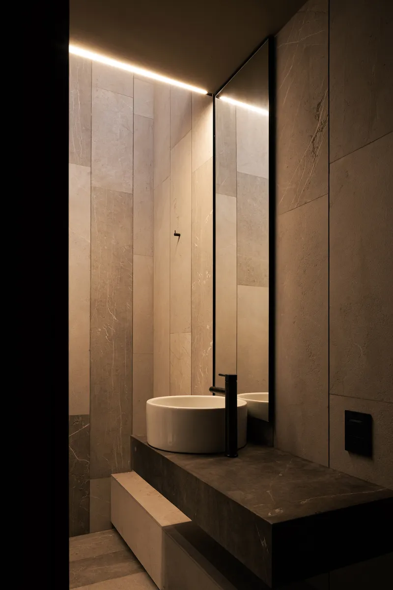 Powder room with vertical stone slab walls and linear ceiling light above round basin