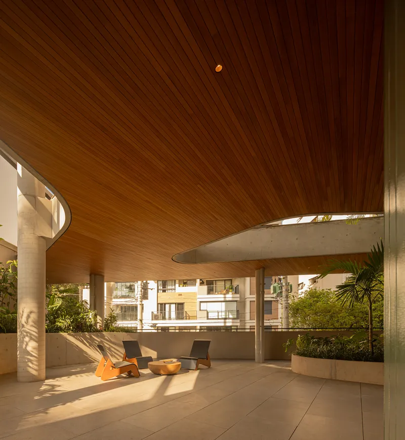 Covered terrace with sculptural timber ceiling, concrete columns, and two chairs in dappled afternoon light