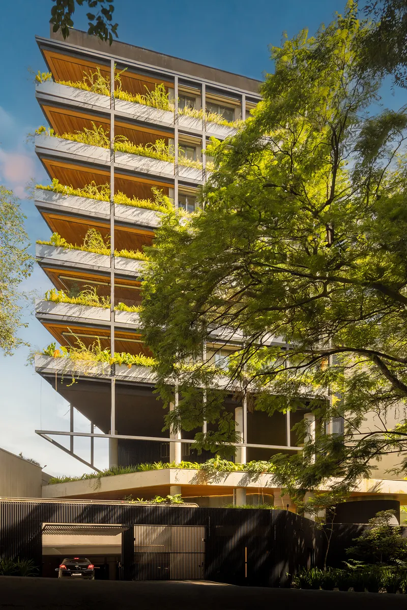 Street view of the stacked facade with planted terraces and a mature tree in afternoon light