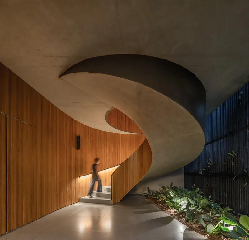 Curved concrete stair with timber-clad walls and a figure ascending past planted beds