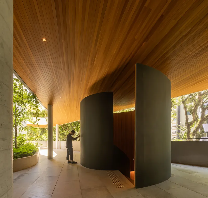 Covered entry lobby with timber slat ceiling and cylindrical partition as a figure approaches