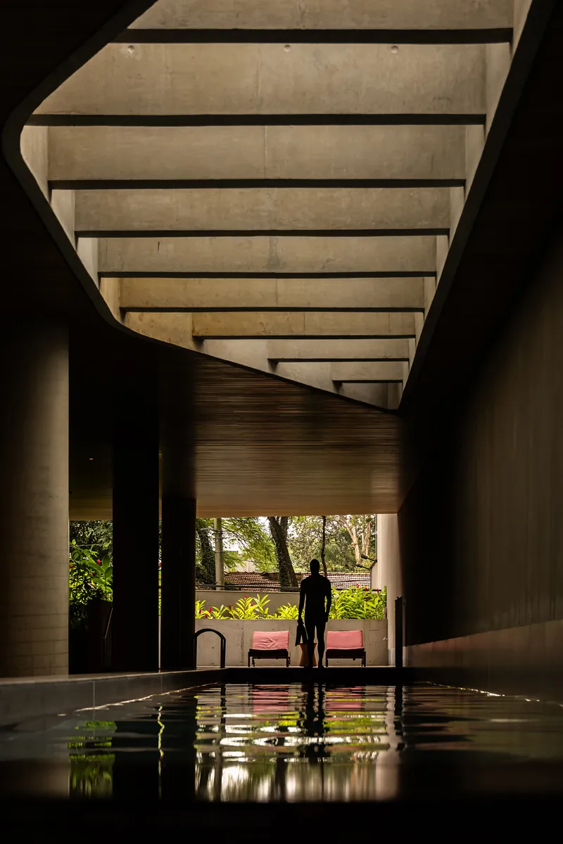 Interior pool with concrete soffit and a silhouetted figure beside outdoor landscape beyond