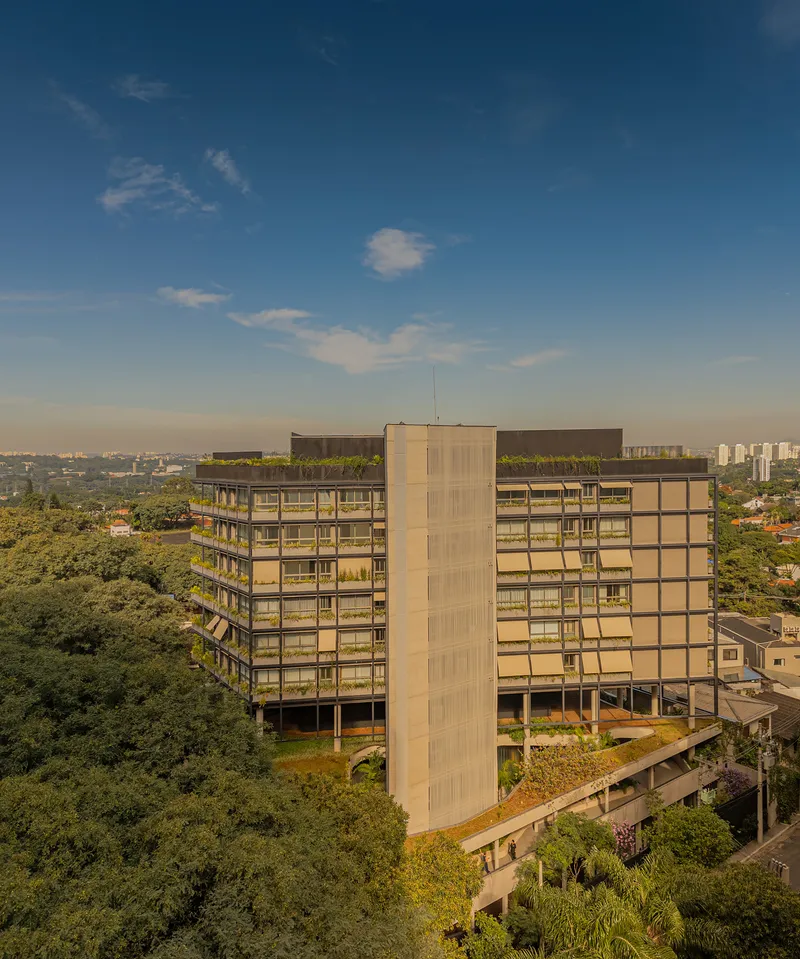 Aerial view of the multistory residential block with planted balconies surrounded by dense tree canopy