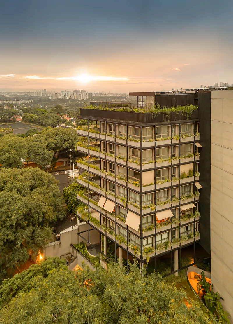 Corner facade with continuous planted balconies stacked vertically beneath rooftop garden at sunset