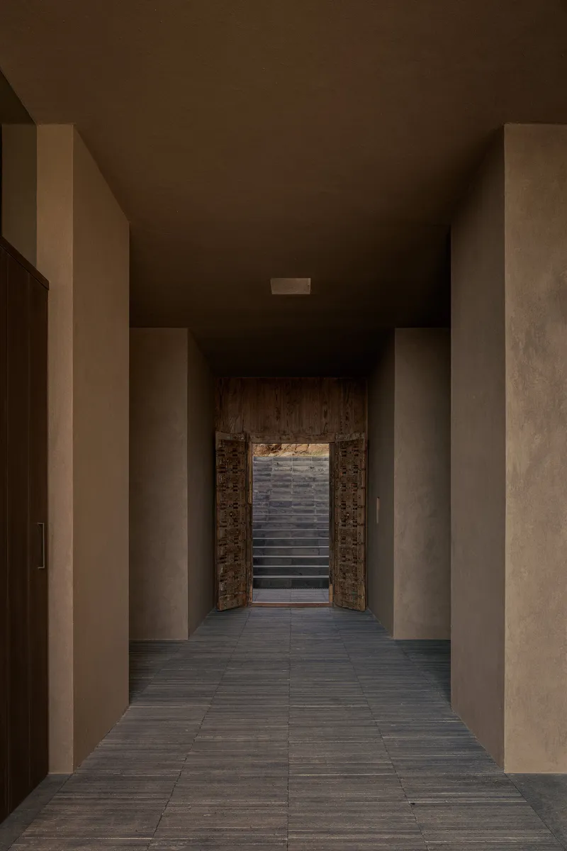 Narrow hallway terminating at carved timber doors opening to exterior steps beyond