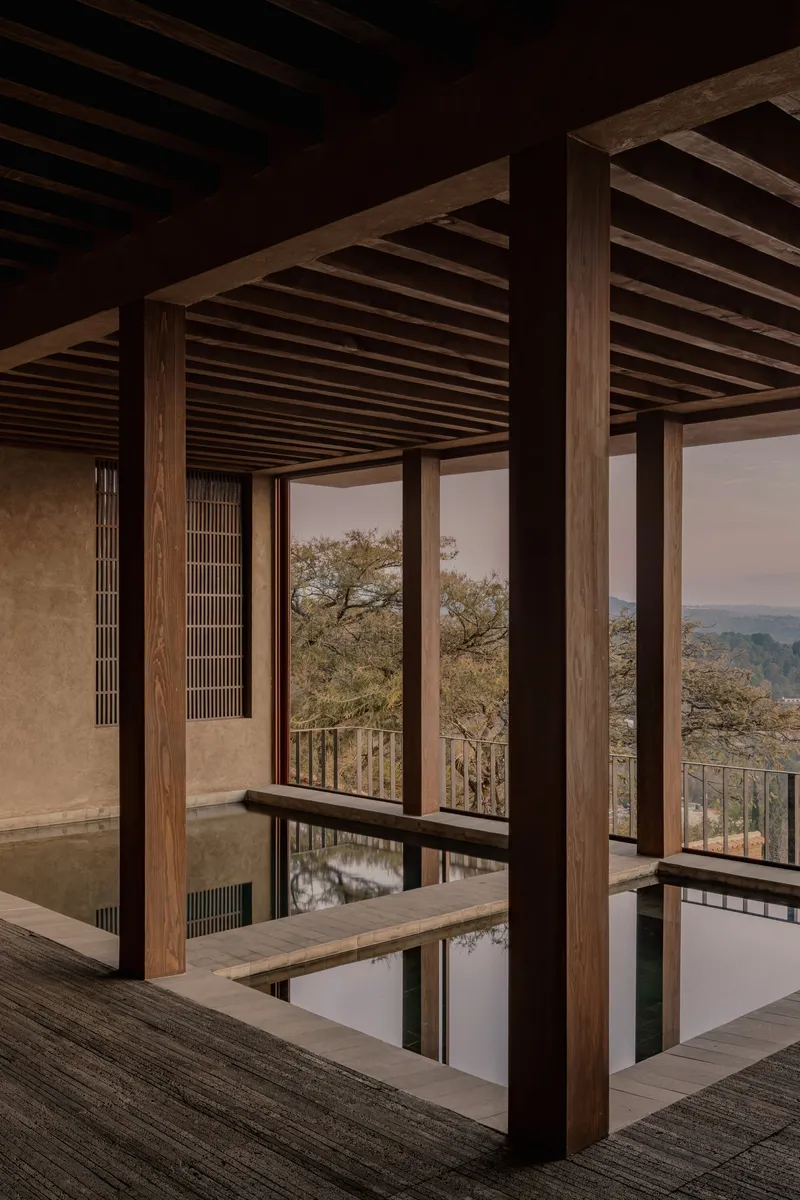 Timber post and beam framework around a reflecting pool with landscape beyond through glass walls