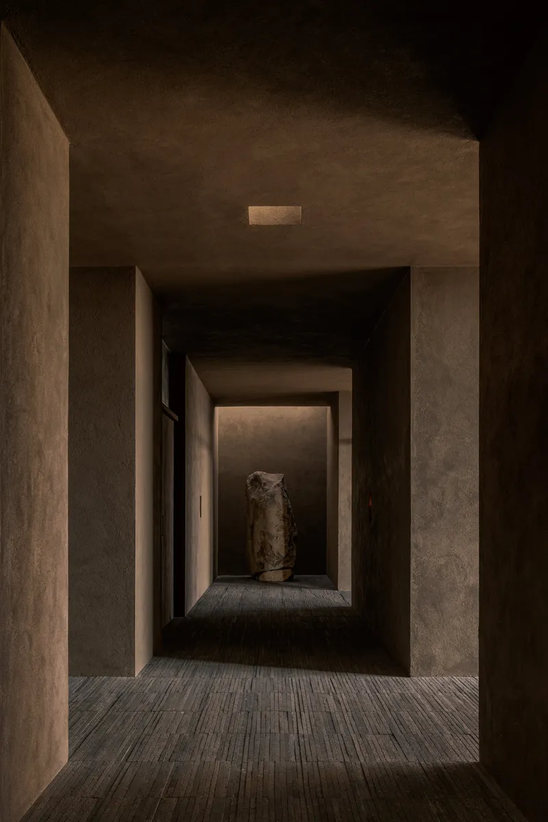 Narrow corridor with timber flooring leading to an illuminated niche displaying a ceramic vessel