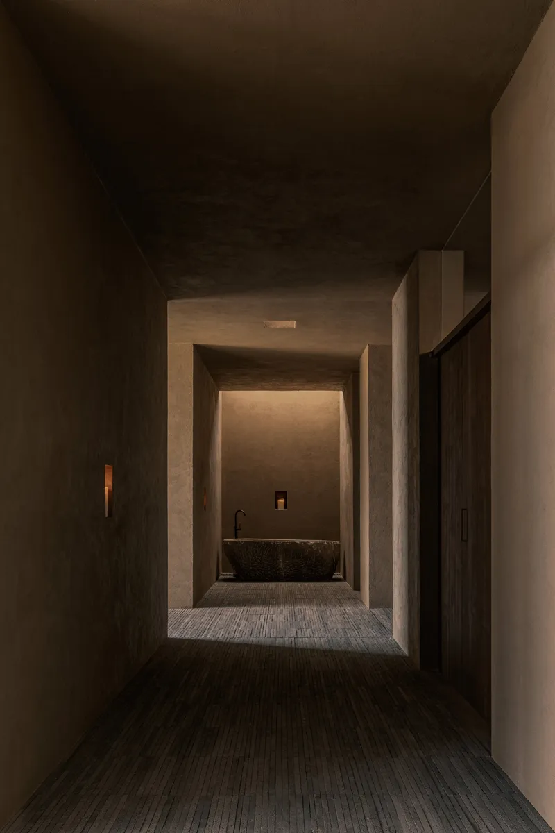 Layered concrete threshold spaces framing a stone basin under concealed ceiling lighting