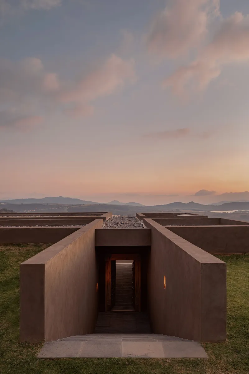 Sunken entrance portal with oxidized metal walls and flanking vertical slits of light at twilight