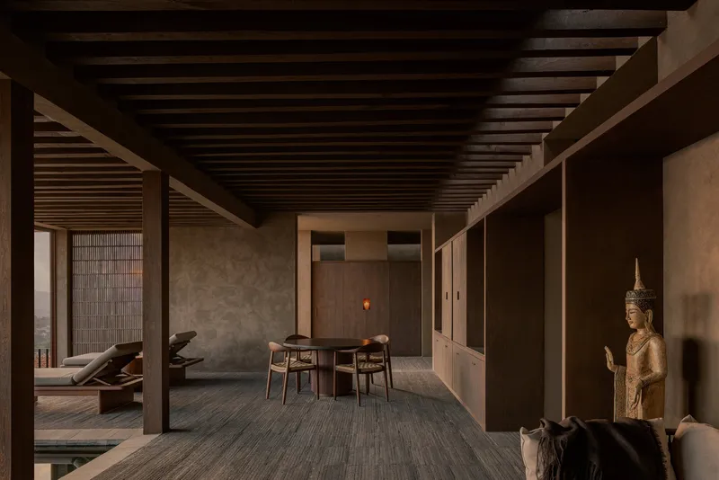 Open-plan living space with timber beam ceiling and Buddha sculpture beside view to courtyard pool