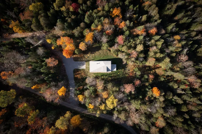 Aerial view of the white gabled roof surrounded by deciduous forest in autumn
