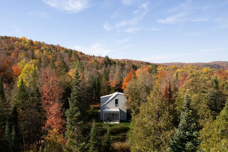 The house nestled in a clearing among mixed forest with fall foliage