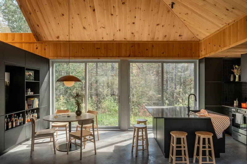 Open kitchen and dining area with knotty pine ceiling and full-height glazing overlooking forest