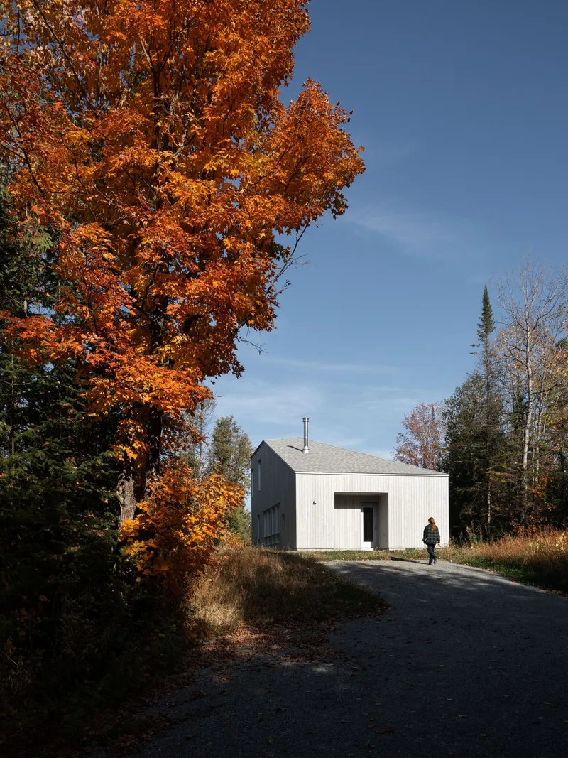 White corrugated metal facade with recessed entry and person walking on gravel path in autumn