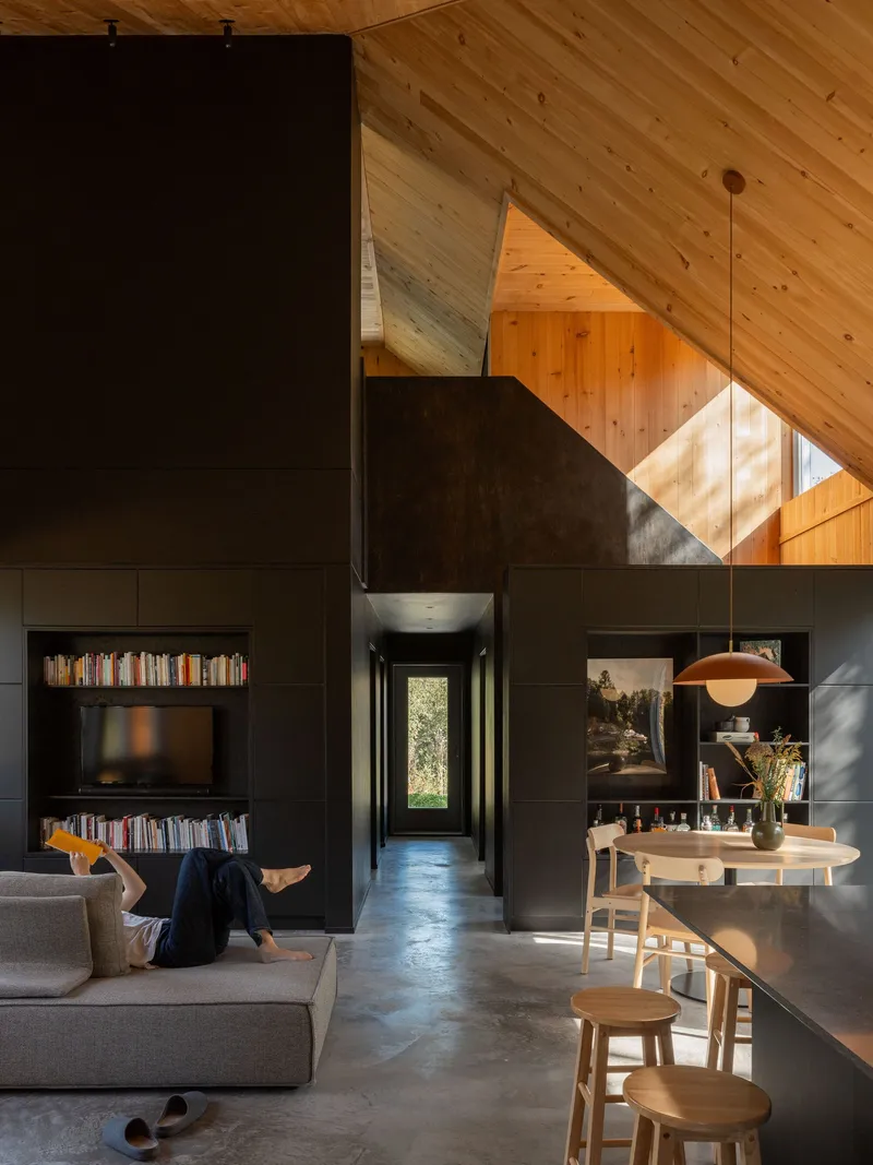 Open interior showing black storage volume under sloped pine ceiling with skylight above dining table