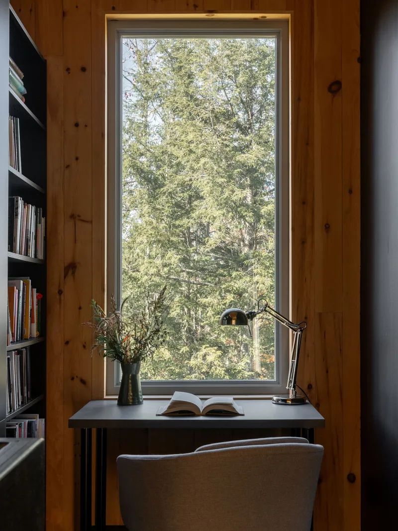 Reading nook framed by knotted pine walls with a tall window overlooking deciduous trees