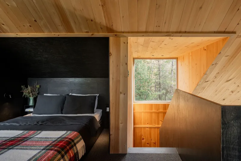 Sleeping loft with black accent wall and angled timber ceiling opening to a window seat