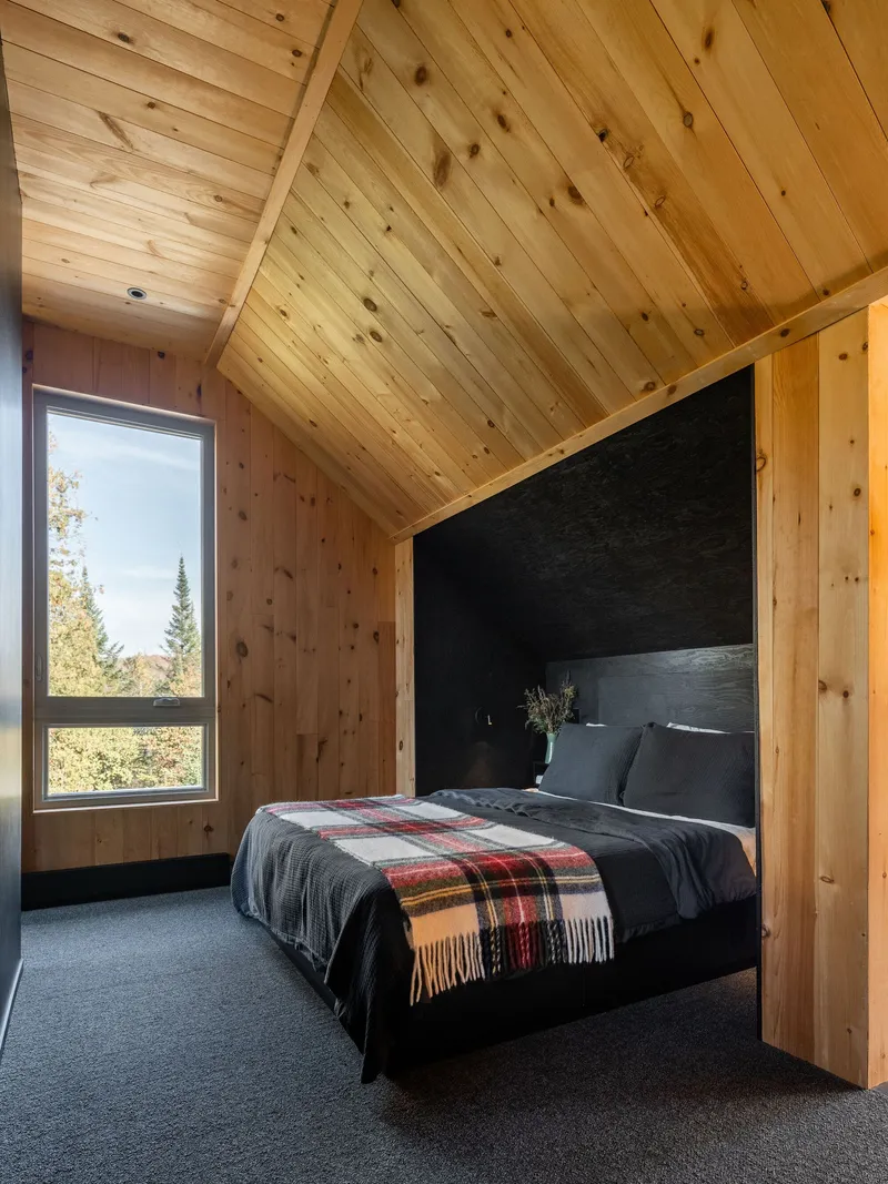 Bedroom with vaulted knotted pine ceiling and corner window framing evergreen forest views