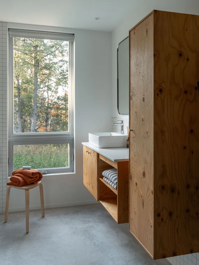 Bathroom vanity in knotted timber beside a stacked window overlooking autumn foliage