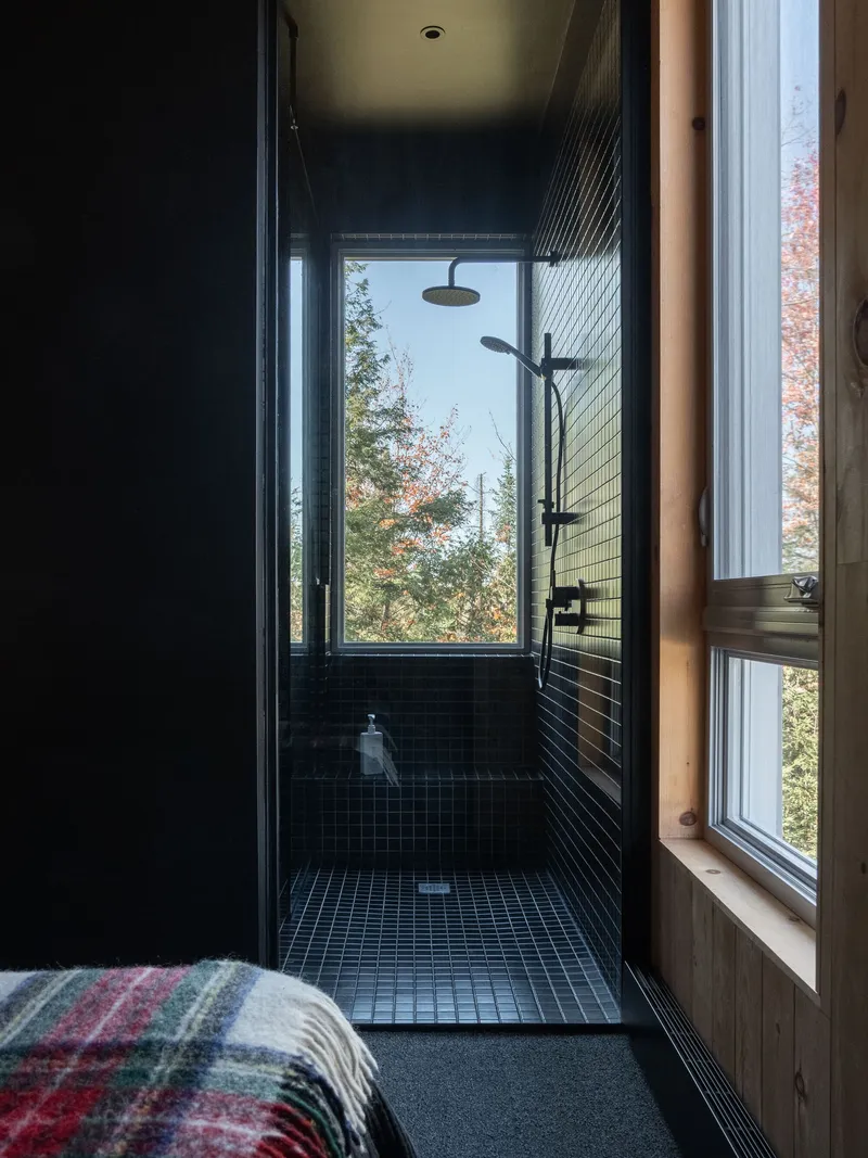 Black tiled shower enclosure with narrow window framing autumn foliage outside