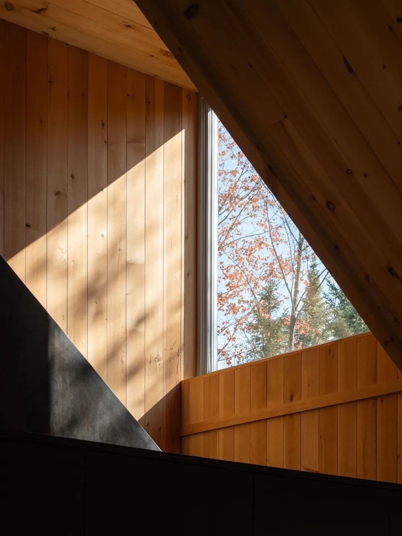 Triangular window cut through timber wall panels with sunlight casting diagonal shadows