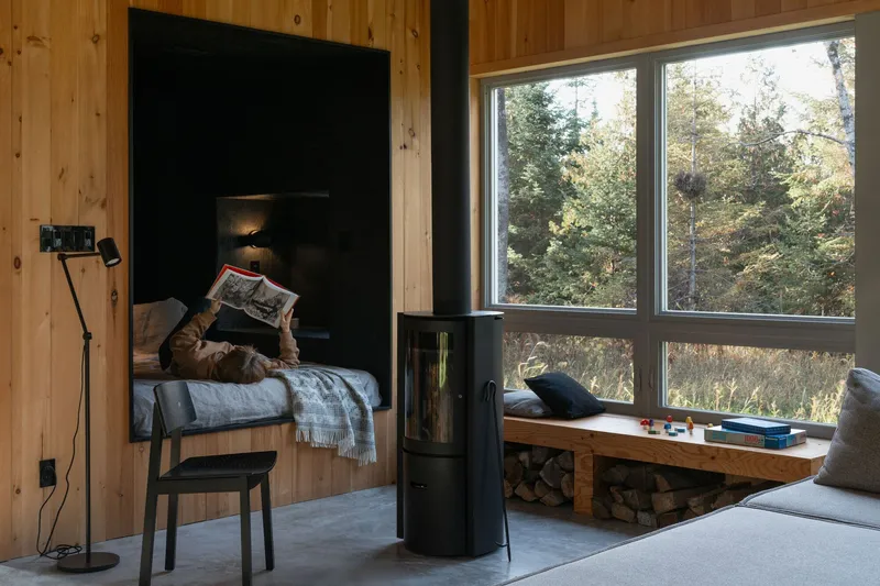 Reading nook with freestanding wood stove and large windows overlooking forested landscape