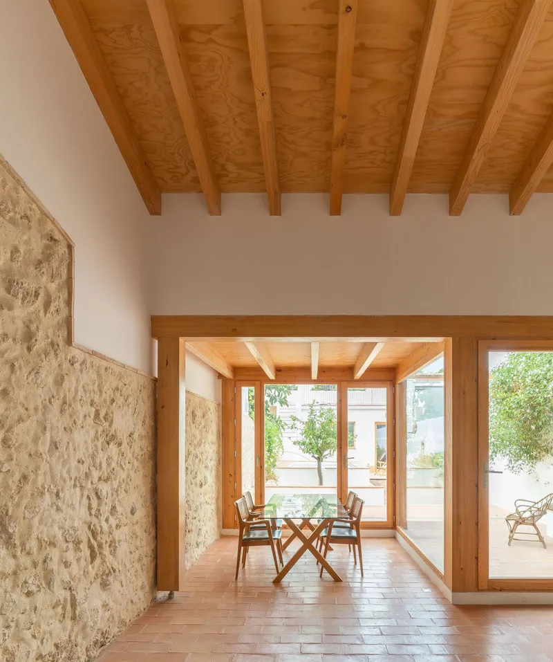 Interior dining space with exposed timber ceiling beams and stone wall opening onto terracotta tile patio