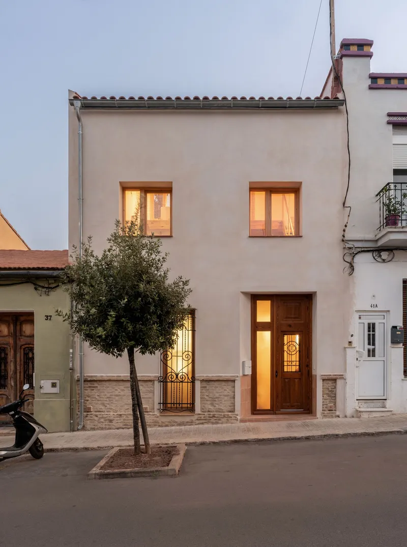 Street facade with illuminated windows and entry door flanked by a street tree at dusk