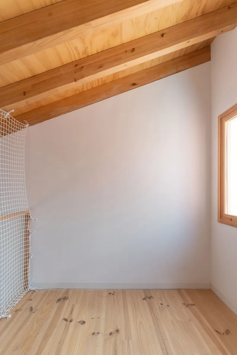 Small room with pine floor, white walls, exposed timber ceiling joists and safety netting at left