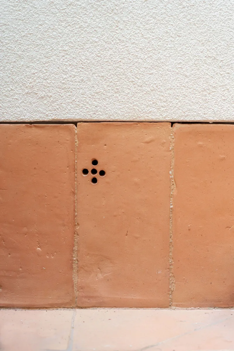 Close-up of terracotta tile joint with four circular weep holes below white rendered wall