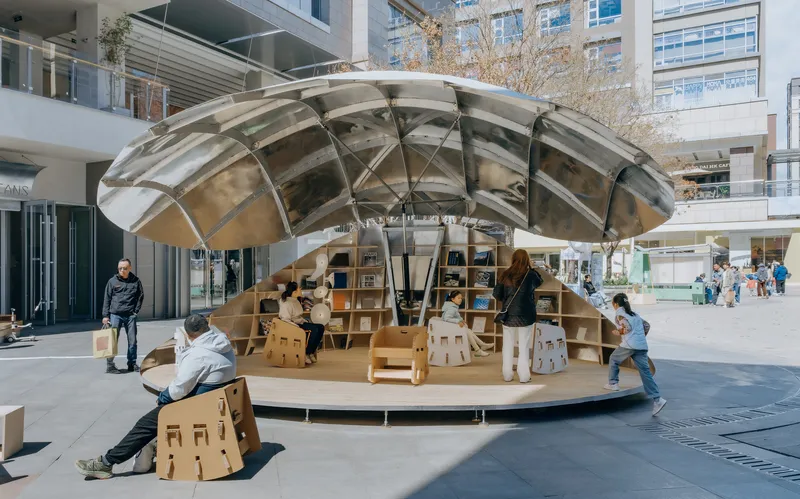 Side view of the circular pavilion showing the dome's structural frame and plywood base with visitors seated