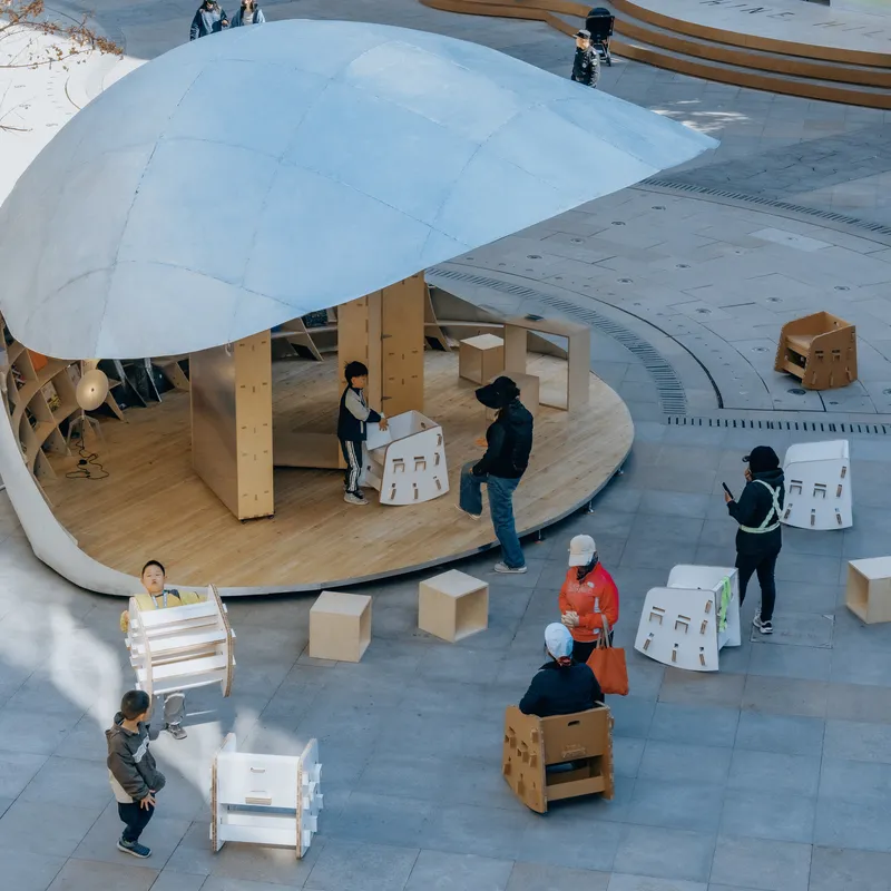 Angled view of visitors interacting with cardboard furniture beneath the dome in the tiled courtyard