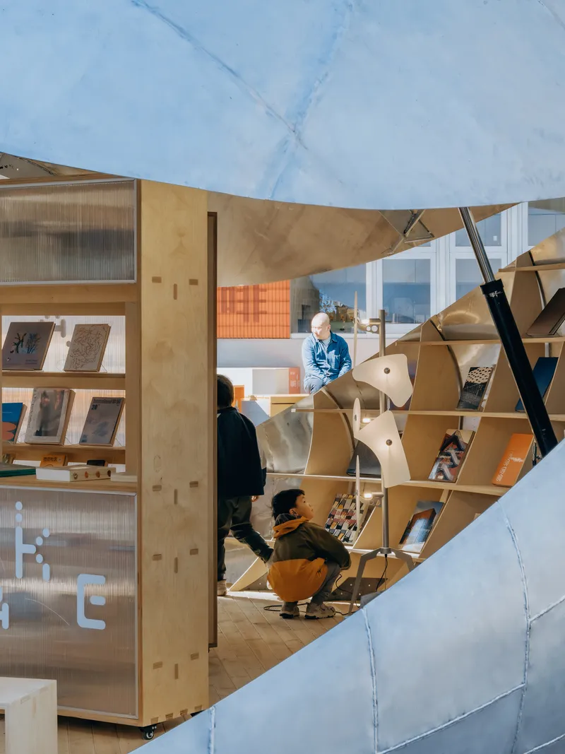 Interior view of plywood shelving with tiered seating beneath a curved translucent dome and visitors browsing