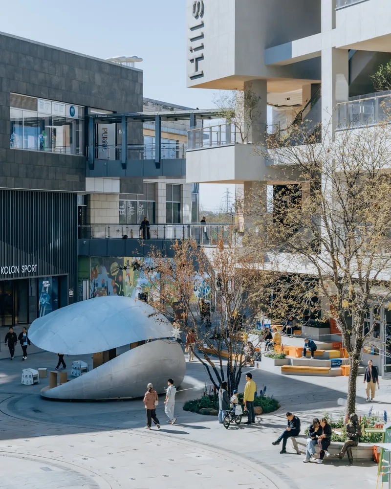 Plaza with white dome pavilion surrounded by pedestrians, bare trees and multi-storey commercial buildings