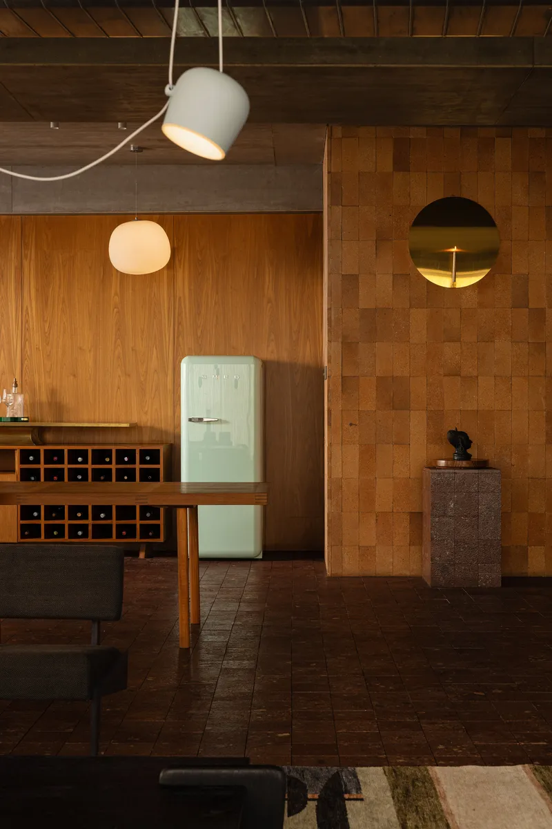 Cork tile wall with oval brass mirror beside a walnut bar and globe pendant
