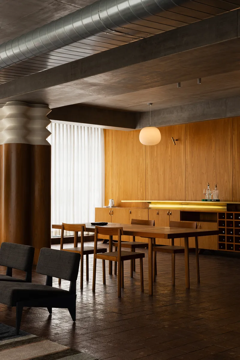 Dining area with timber credenza, ridged bronze column, and spherical pendant light beneath exposed ductwork
