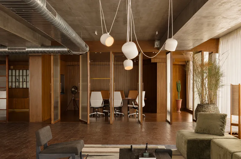 Open workspace with glass-walled meeting room, cluster of globe pendants, and potted grasses by curtains